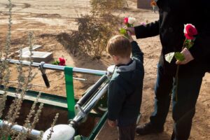 Opioid overdose funeral; father and son throwing roses into grave